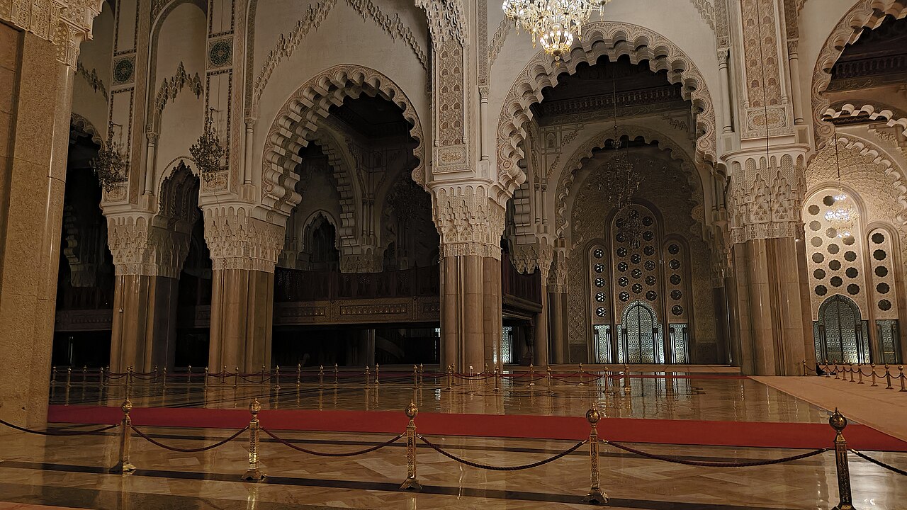 De gebedszaal van de Hassan II-moskee met marmeren zuilen, hoefijzerbogen en kroonluchters