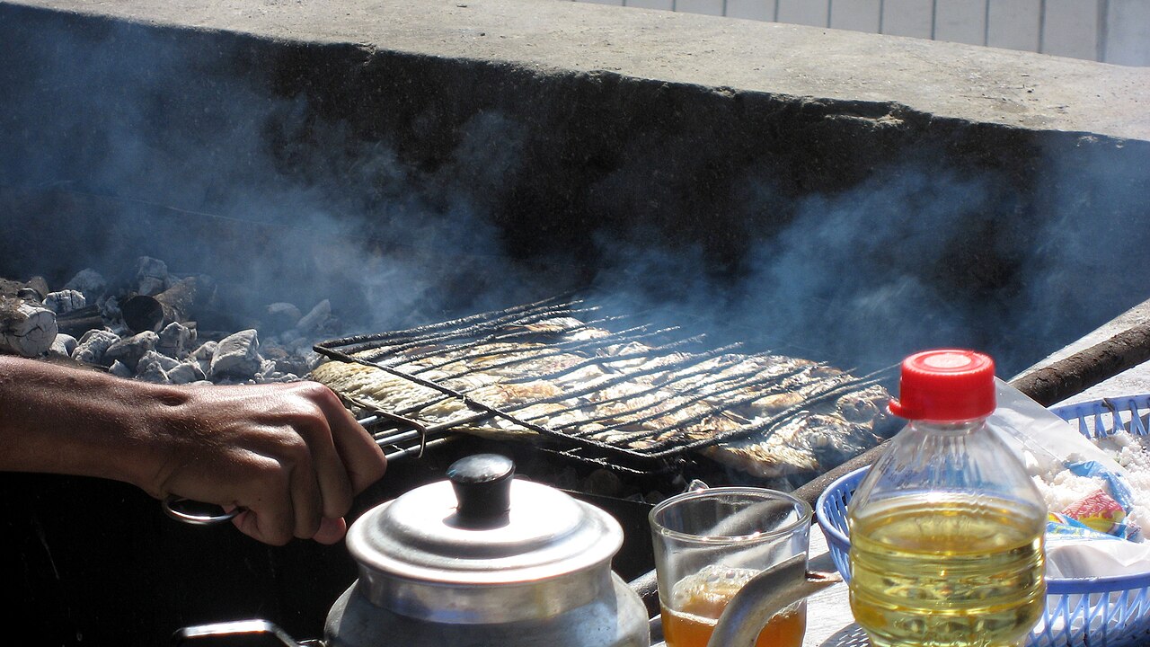 Sardines op een houtskoolgrill met een theepot en glas muntthee ernaast